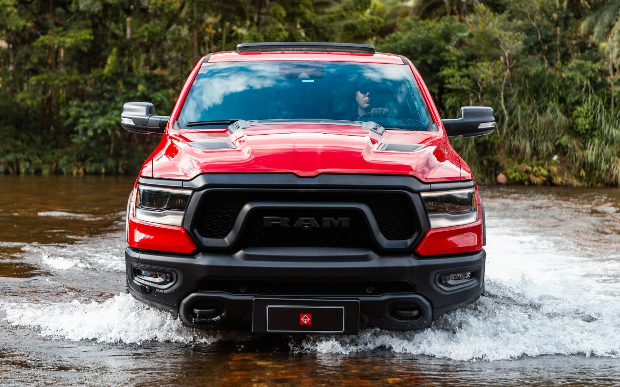 A red fifth-generation Ram 1500 Rebel driving through a shallow river