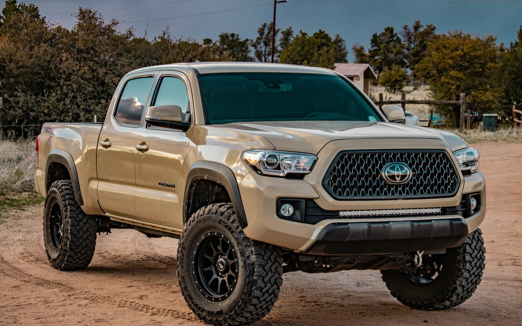 A tan third-generation Toyota Tacoma Double Cab on a dirt lot